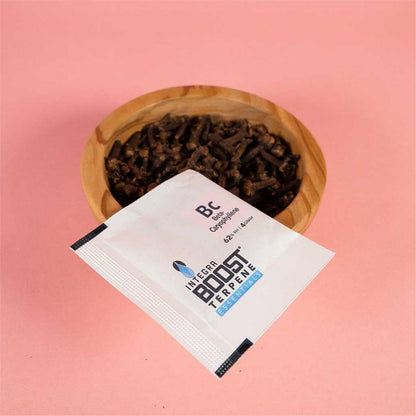 Integra Boost Terpene Essentials Beta-Caryophyllene Bc 62% RH 4g Feuchtigkeitspad vor Holzschale mit Gewürznelken, rosa Hintergrund
