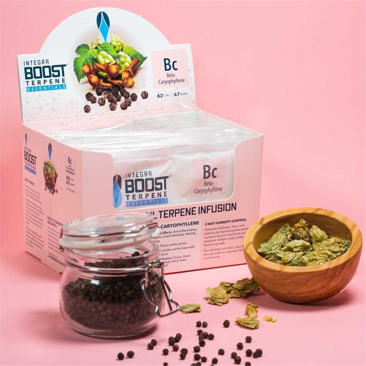Integra Boost Terpene Essentials Beta-Caryophyllene Bc 62% RH 67g Display-Box mit Glasgefäß Pfefferkörner und Holzschale Hopfen, rosa Hintergrund