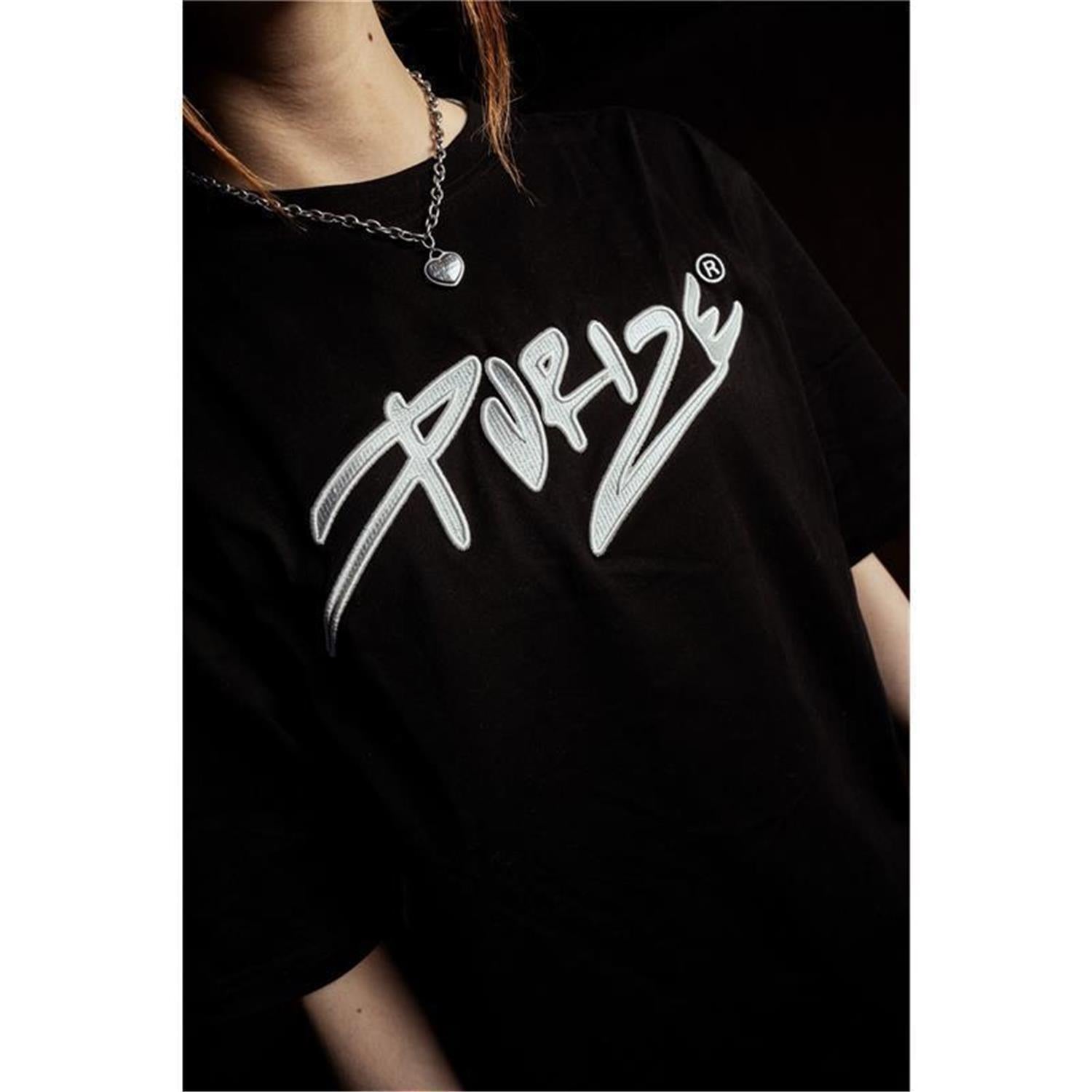 PURIZE T-Shirt in Schwarz mit gesticktem Logo, von Frau im Oversize-Fit vor Graffiti-Wand getragen, Streetwear-Look